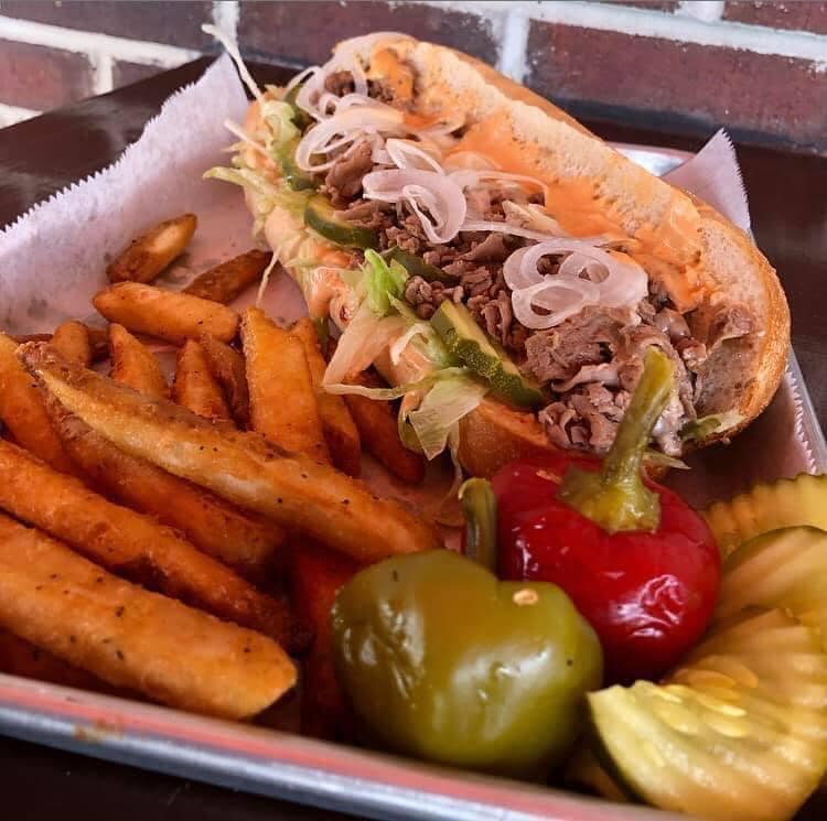 A cheesesteak with fries, hot peppers, and pickles.