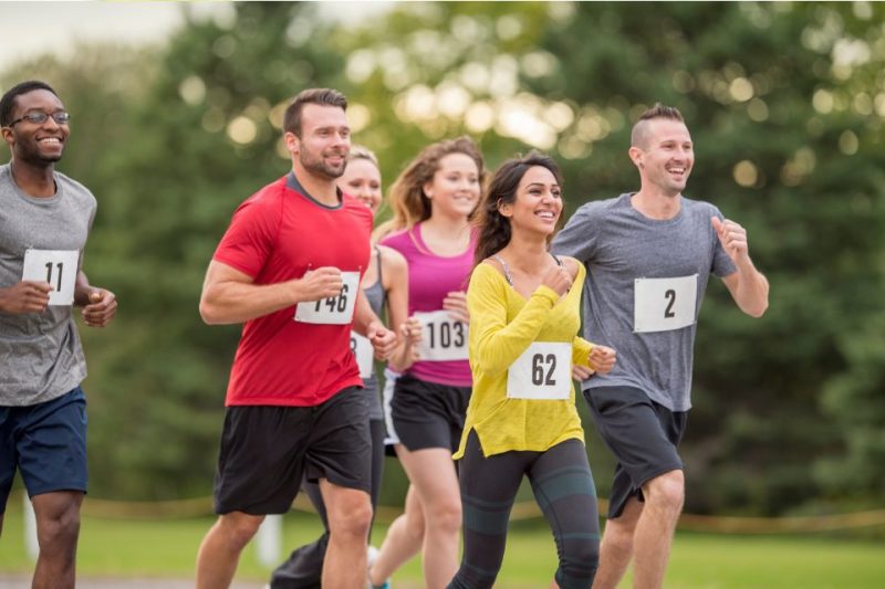 Six runners wear 5k race numbers while happily running a race on a sunny day.