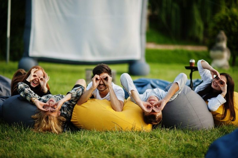 Young multi ethnic group of people watching movie at poof in open air cinema.