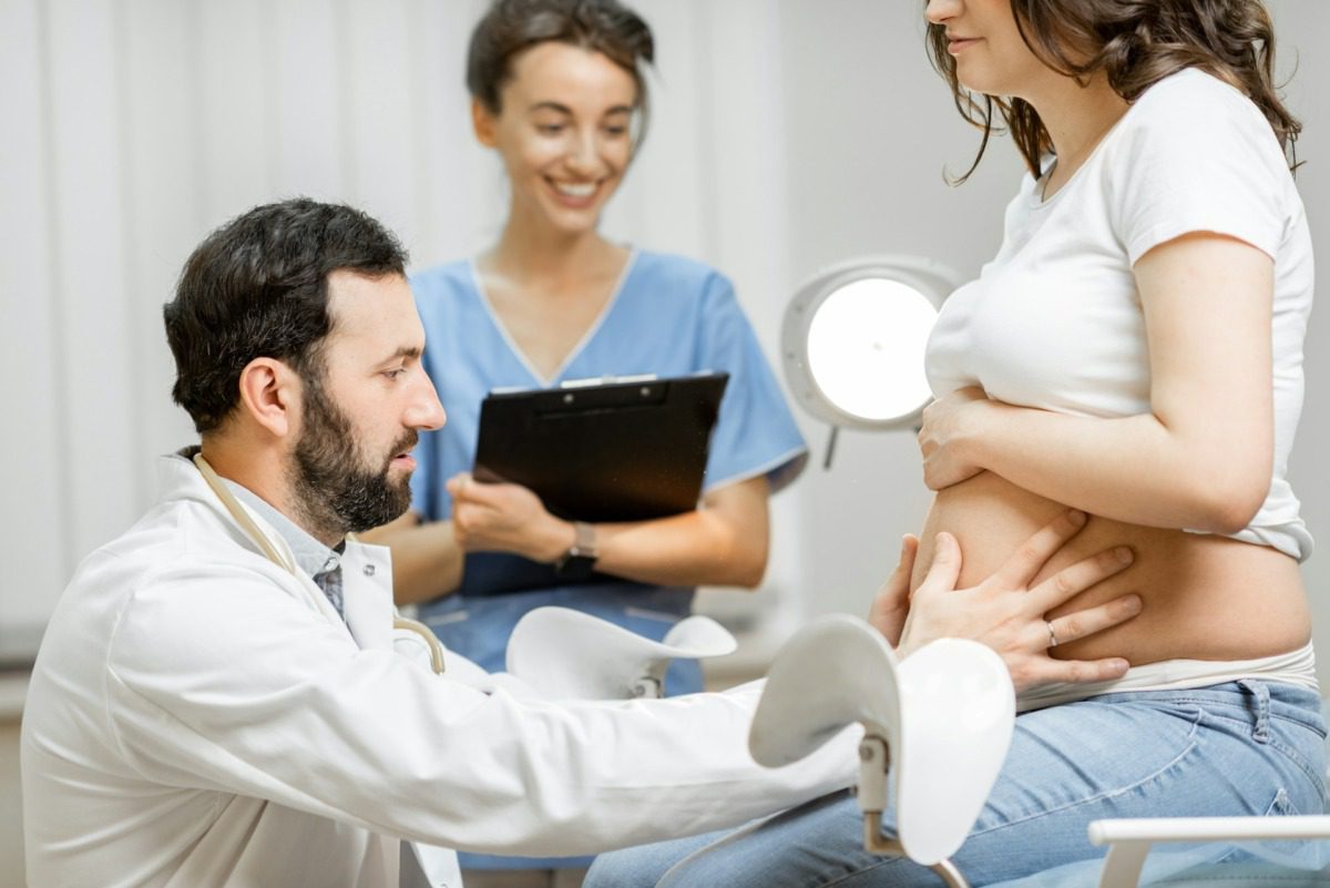 Young woman receiving a pregnancy check up with a male doctor and female nurse.