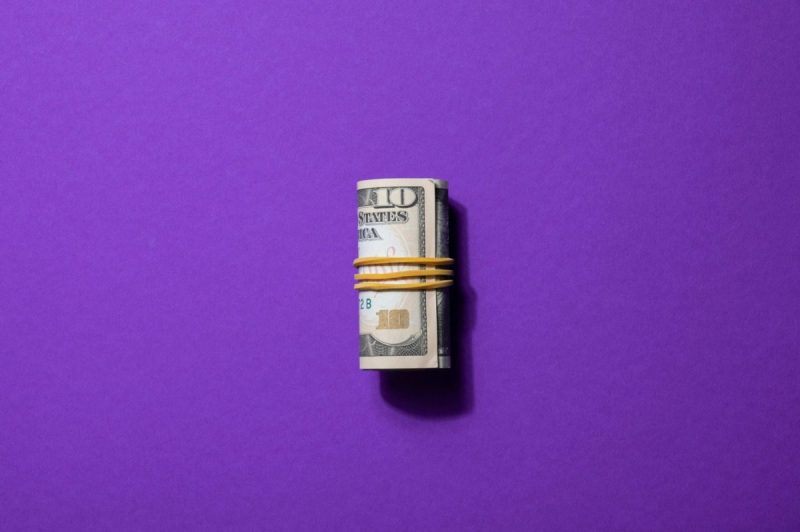 Roll of dollar bills against a purple background.