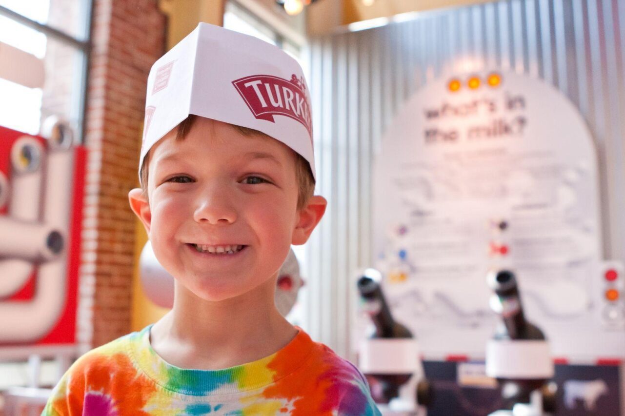 a little boy smiles while wearing a turkey hill experience hat inside the ice cream shop